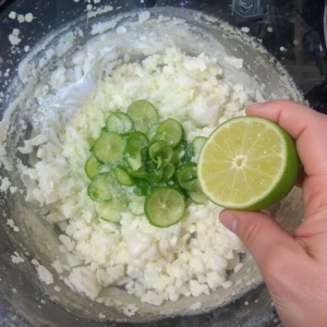 Fresh lime juice being squeezed into a bowl of guacamole, adding a zesty flavor and preventing browning.