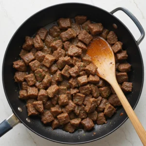 Beef sizzling in a hot skillet, developing a golden-brown crust for added flavor and richness.