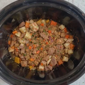 A slow cooker filled with sliced beef, chopped vegetables, and a rich sauce, ready to be slow-cooked to perfection.