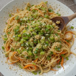 A beautifully plated cucumber salad in a bowl, topped with sesame seeds, sliced green onions, and a drizzle of vibrant red chili oil. Crushed peanuts are sprinkled over the top for added crunch. The fresh, glistening cucumbers contrast with the garnishes, making the dish visually appealing and full of flavor. Chopsticks rest beside the bowl, ready for serving.